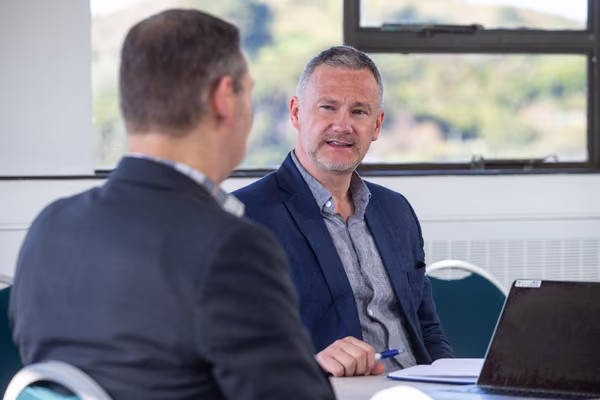 Two men talking whilst sitting in front of a laptop