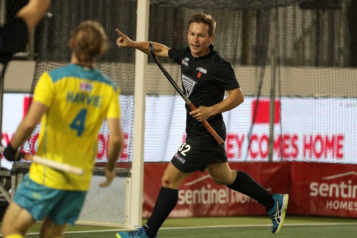 Two teams playing field hockey, with one player scoring a goal and celebrating