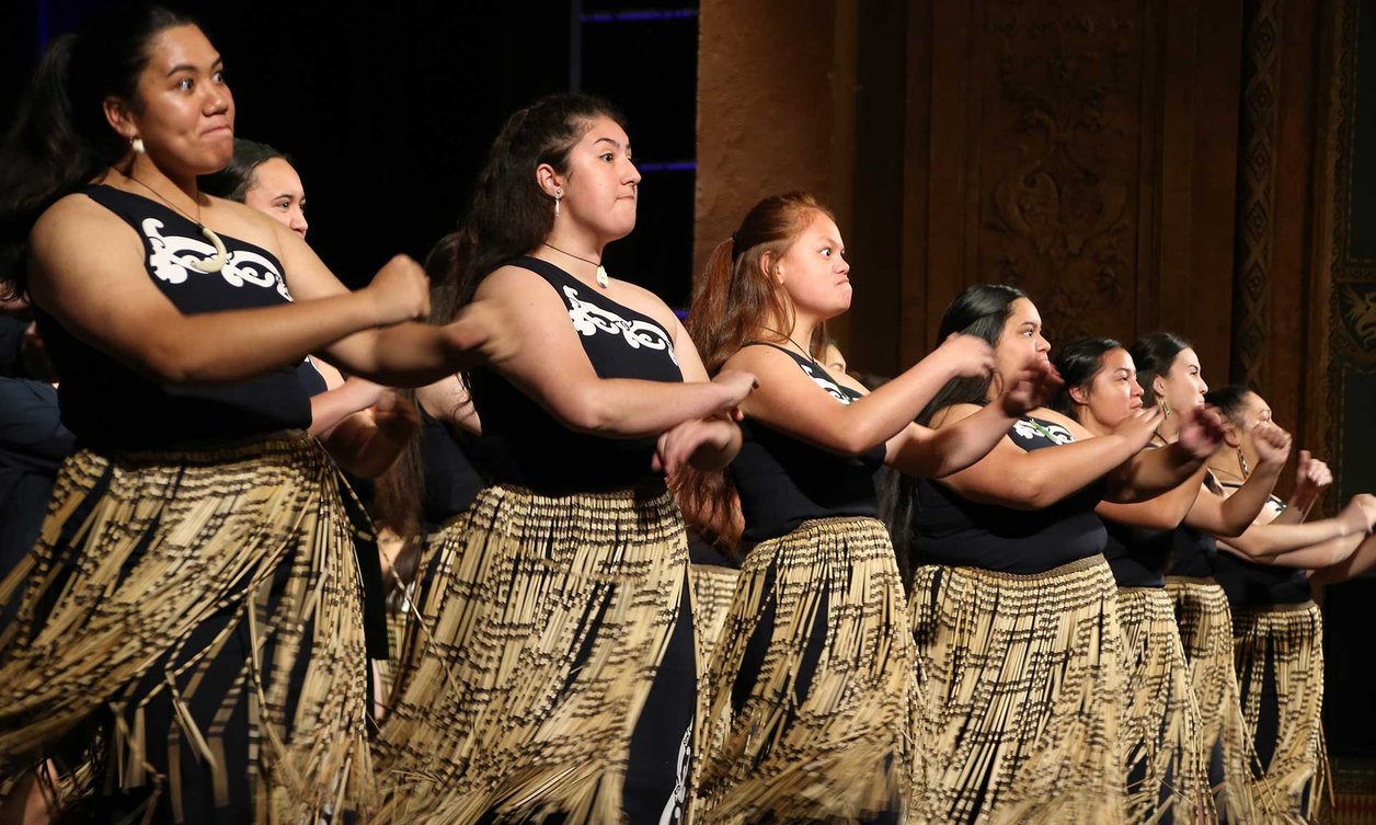 Group of women performing a waiata, dressed in full traditional Maori costume
