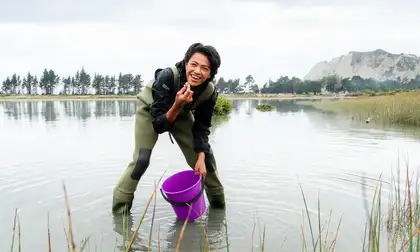 Young person holding a bucket inspects an item from the waterway.