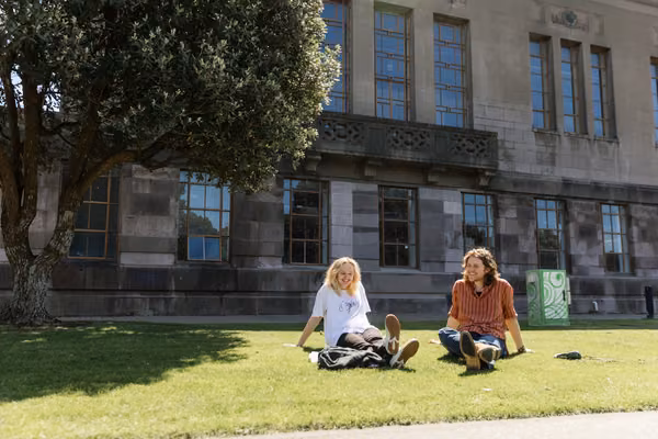 Two students sitting on grass outside at Massey campus in Wellington