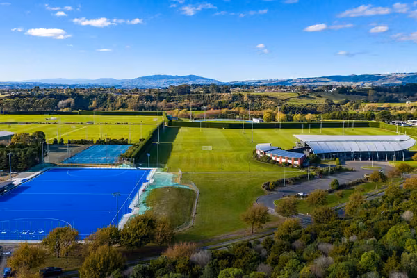 View from the sky of the sport and rugby institute building which looks like a silver fern shape, surrounded by green rugby and sports fields.