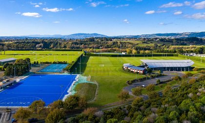 View from the sky of the sport and rugby institute building which looks like a silver fern shape, surrounded by green rugby and sports fields.