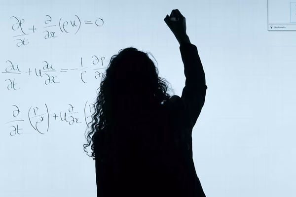 Silhouette of person writing equations on whiteboard