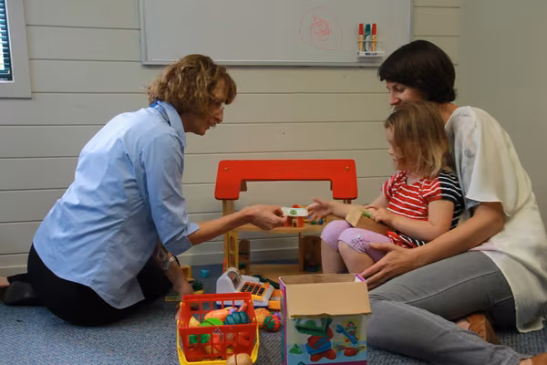 A mother, child and a specialist playing with toys.