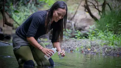 Smiling person standing in river collecting water samples