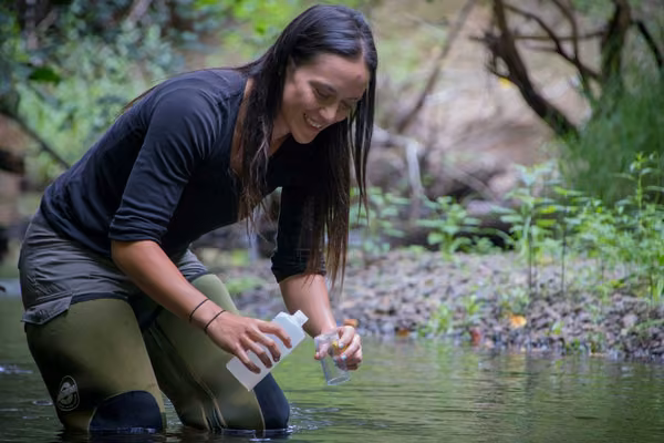 Smiling person standing in river collecting water samples