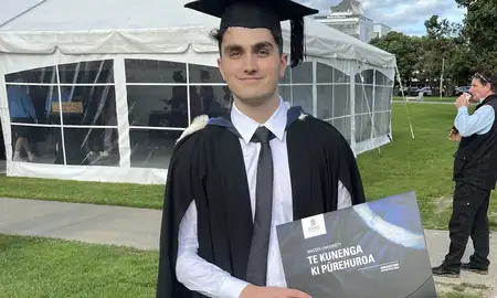 Owen on his graduation day in a cap and gown holding his degree.