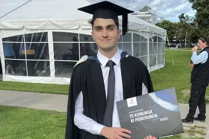 Owen on his graduation day in a cap and gown holding his degree.