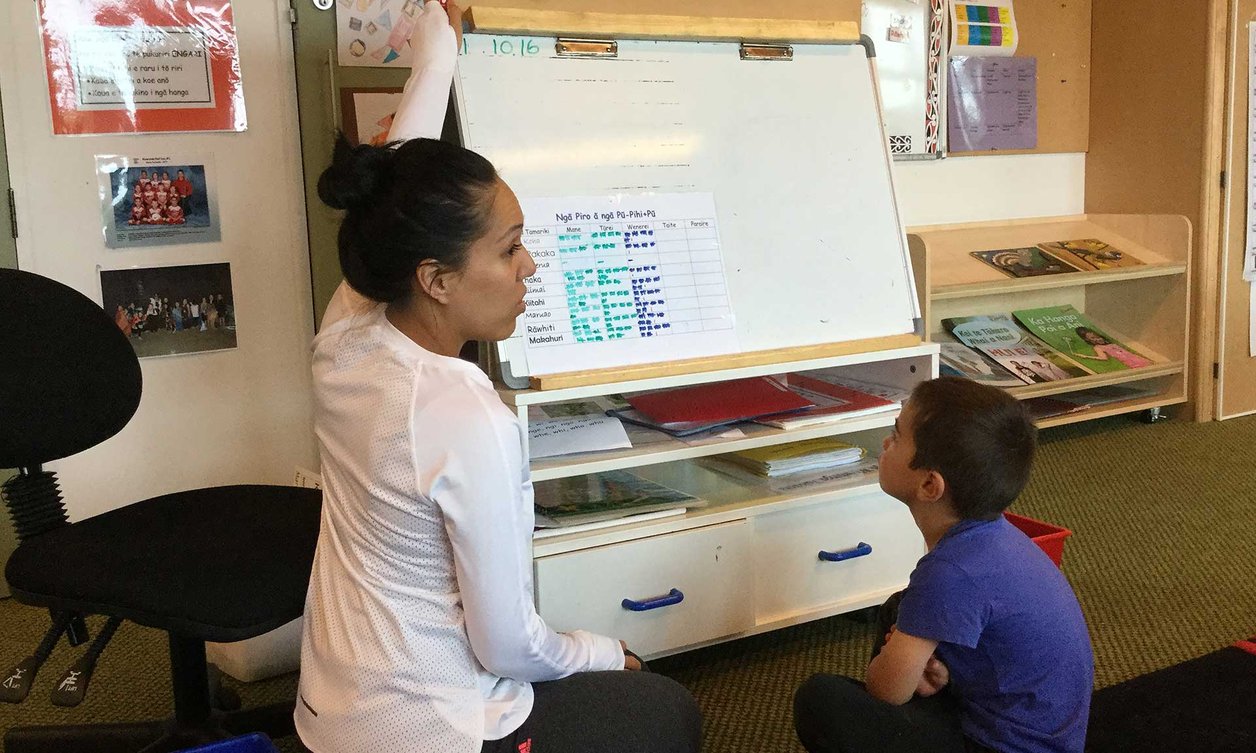 Student teacher sitting on the floor with a young boy, using a whiteboard to teach te Reo
