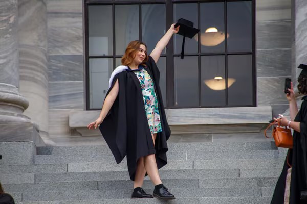 Graduate flourishes trencher on the steps of the Wellington art museum building