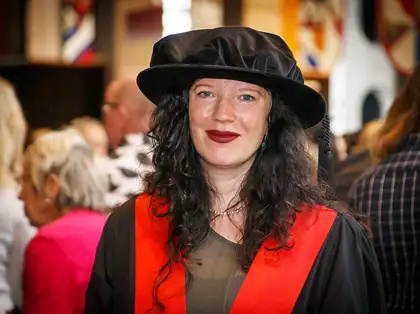 Woman with brown curly hair wearing a graduation cap and gown and smiling.