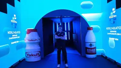 Sam standing arms crossed next to two large Yakult bottles at World Aquatics champs