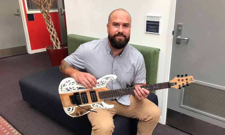 Close-up of Sean Rasmussen seated, strumming a guitar with Maori motifs on it