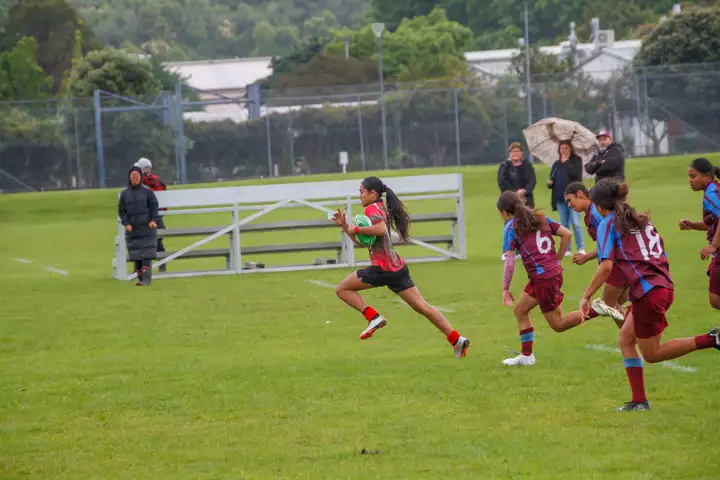 girl running across field with rugby ball under arm