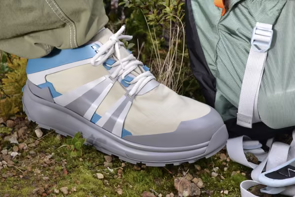 Grey Beige Blue shoe for hiking posed on rocks and moss with backpack