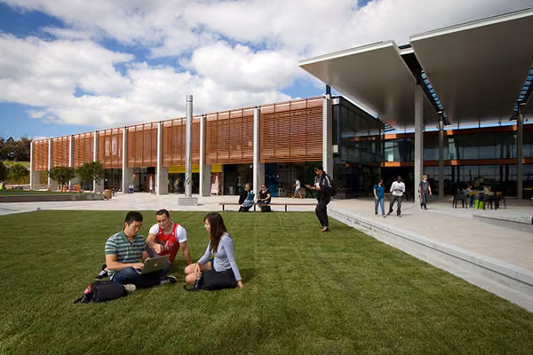Students sitting on grassy area in front of architectural building.