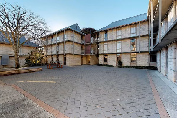 Exterior of City and Egmont Court accommodation with a paved courtyard, and seating under a deciduous tree, in the foreground