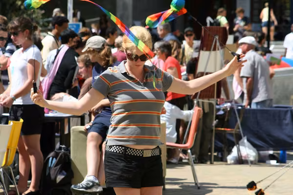 Student twirling two narrow rainbow flags, with a crowd of students in the background