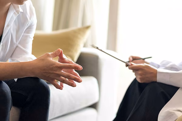 Person leaning forward while seated on a couch, while counsellor holds clipboard