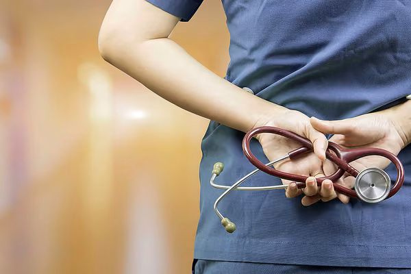 Health worker in uniform standing, and holding a stethoscope behind their back