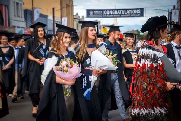 Graduation procession focussing on two people smiling, holding large bouquets of flowers
