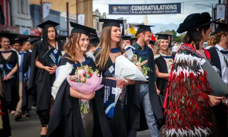 Graduation procession focussing on two people smiling, holding large bouquets of flowers