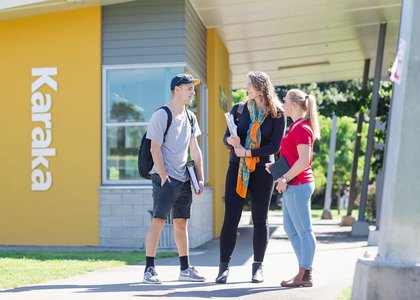 Three people standing outside Karaka accommodation on a sunny day