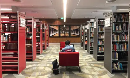 A student sitting on a chair between the stacks of Massey's Auckland Library