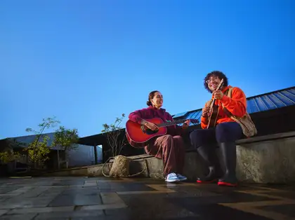 Two students sitting outside playing guitar