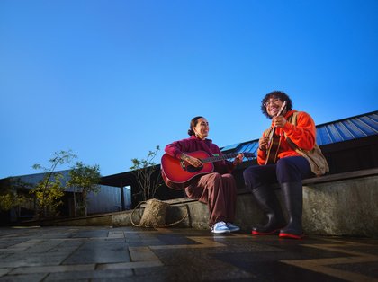 Two students sitting outside playing guitar