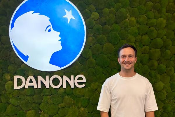 man in white shirt smiling in front of green wall and danone