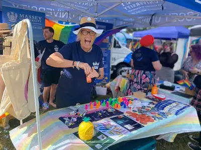 One person grinning on a summer day. They are behind a rainbow advocacy stall