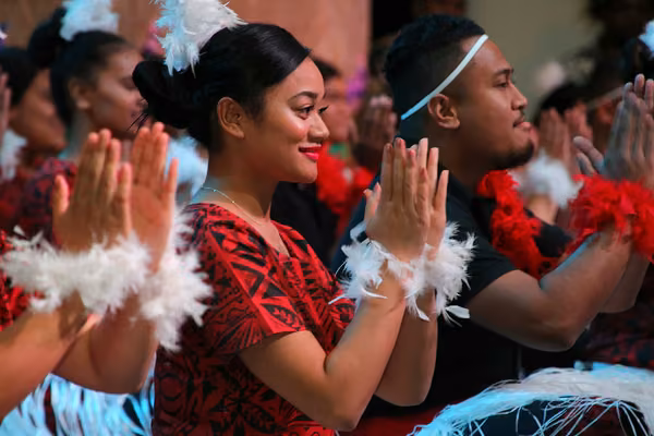 Close-up of person clapping while seated as part of a group giving a traditional Pacific performance