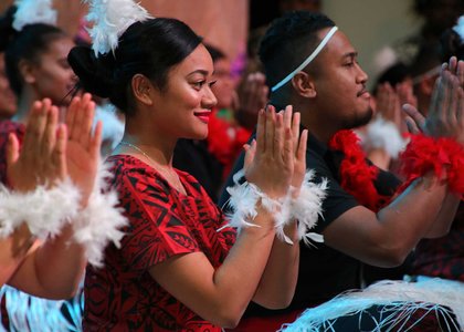 Close-up of person clapping while seated as part of a group giving a traditional Pacific performance