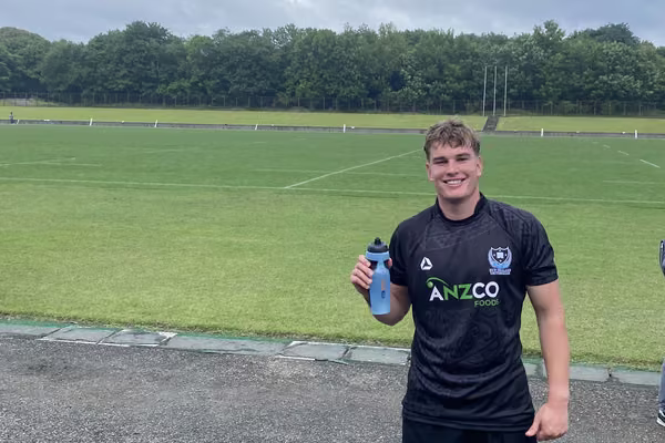 Man in rugby kit standing in front of field holding water bottle
