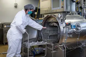 Woman in protective clothing loading a rack into a machine.