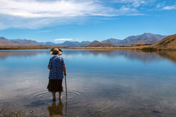 Woman standing in the lake looking out over the water to the mountains beyond.