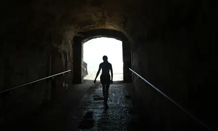 Woman walking through dark tunnel towards light.